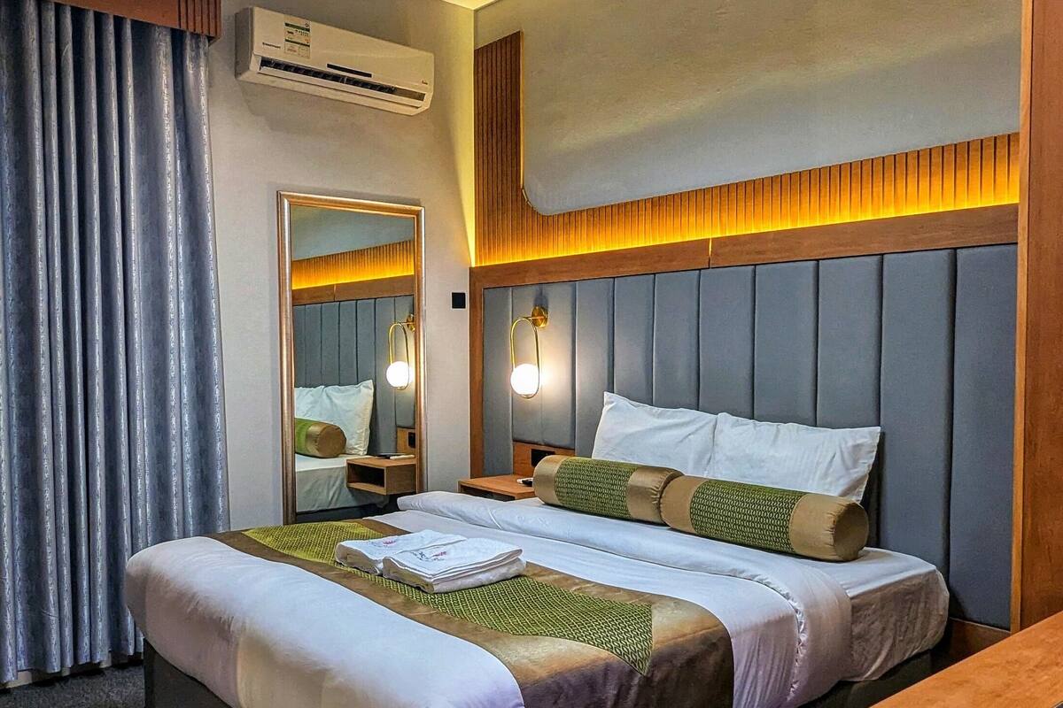 Une chambre d’hôtel moderne avec un grand lit, une tête de lit en bois, une table de chevet, un miroir et un luminaire au plafond.