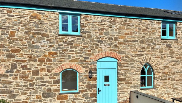 Un bâtiment en pierre avec une porte bleue, deux fenêtres en arc de cercle et une petite enseigne au-dessus de la porte.
