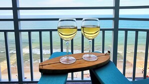 Zwei Gläser Weißwein auf einem Holztablett auf einem Balkon mit Blick auf den Ozean.