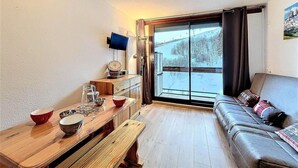 A cozy living room with a wooden table, a sofa, and a large window with a view of a snowy landscape. - 100m from ski slopes, 11st floor, swimming pool, tv, ski locker, 22m², Le Corbier (Le Corbier)