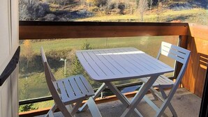 A balcony with a table and two chairs, overlooking a hilly landscape with trees and power lines. - 100m from ski slopes, 11st floor, swimming pool, tv, ski locker, 22m², Le Corbier (Le Corbier)