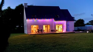 A modern house with a flat roof, large windows, and a covered patio area with outdoor furniture. - Exceptional House for Rent in Finistère between Wild Beaches and Modern Comfort (Landunvez)