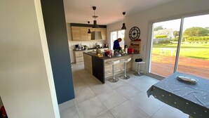 A modern kitchen with a large island, bar stools, and a dining table with a pie. - Exceptional House for Rent in Finistère between Wild Beaches and Modern Comfort (Landunvez)