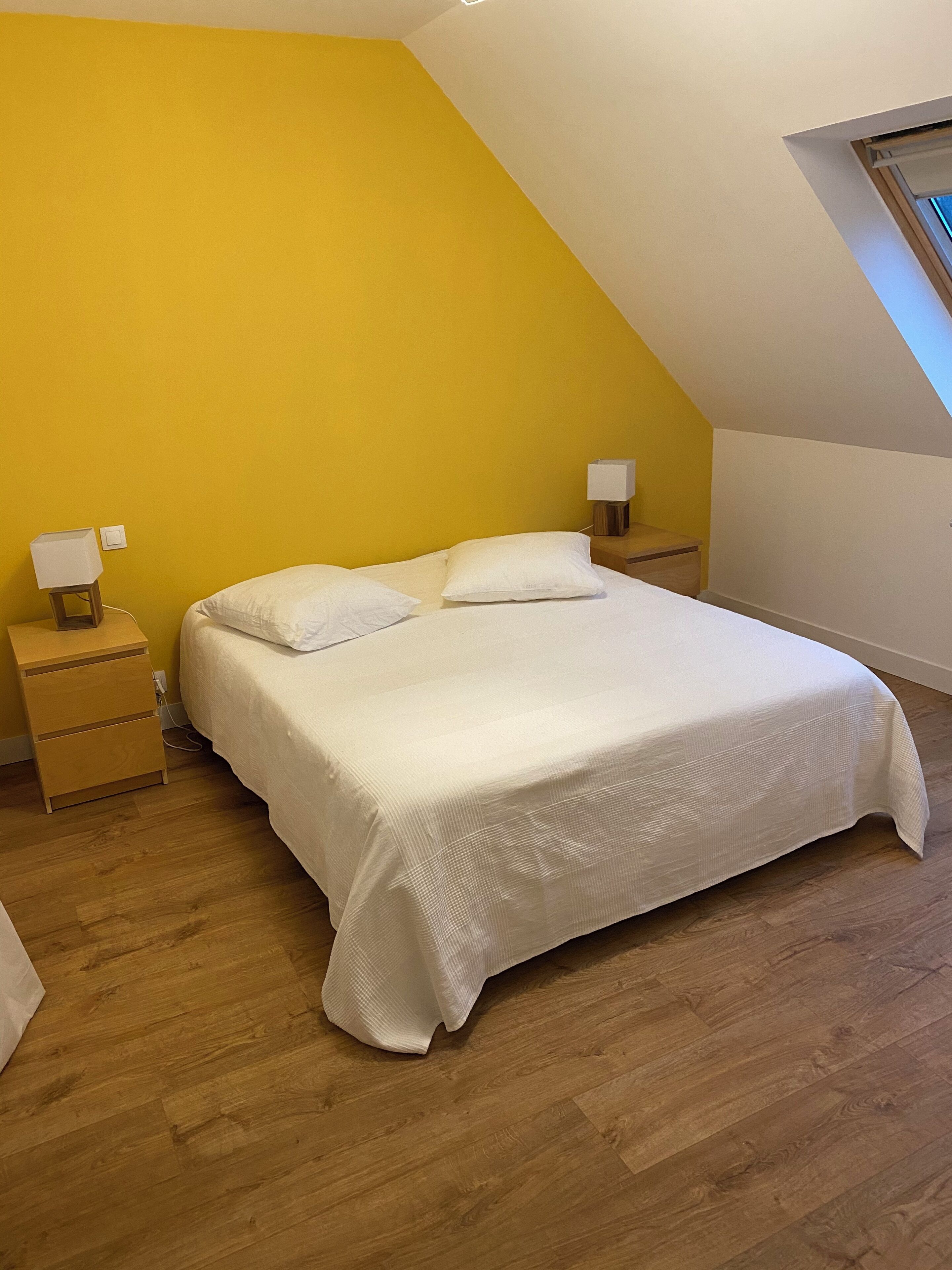 A bedroom with a bed, wooden nightstands, and a sloped ceiling.