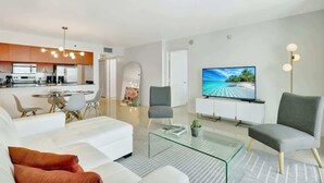 Una sala de estar moderna con una mesa de centro de vidrio, sofás blancos y un televisor de pantalla plana.