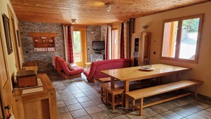 Ein gemütliches Blockhauskamin mit einem Holzespeisesaal, Bänken, einer Steinwand, einem Fernseher und einem roten Sessel.