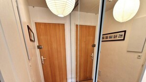 A hallway with wooden flooring, a glass door, and a mirror reflecting the door and a light fixture. - 20m from ski slopes, Ground floor, view ski slopes, balcony, tv, ski locker, 32m², Valfréjus (Valfréjus)
