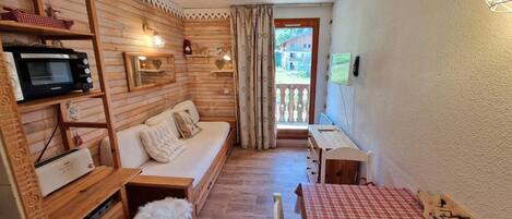 A cozy room with a wooden interior, a sofa, a small table, a microwave, and a view of the outside.