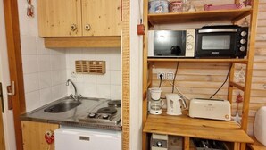 Una cocina compacta con gabinetes de madera, estufa integrada, pileta, microondas, tostadora y un refrigerador pequeño.