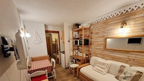 Una habitación acogedora con un sofá de madera, una mesita, una silla, un estante de madera y un espejo en la pared.