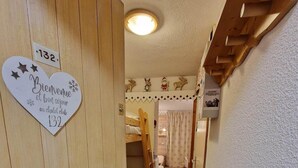 A narrow wooden hallway with a bunk bed and a bunk ladder, a sign reading "Bienvenue et bon séjour au chalet club 132", and a ceiling light.