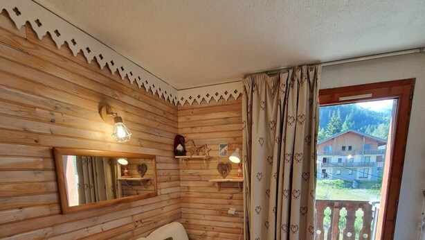 Una habitación acogedora con pared de madera, un sofá con cojines, un espejo y una ventana con cortinas.
