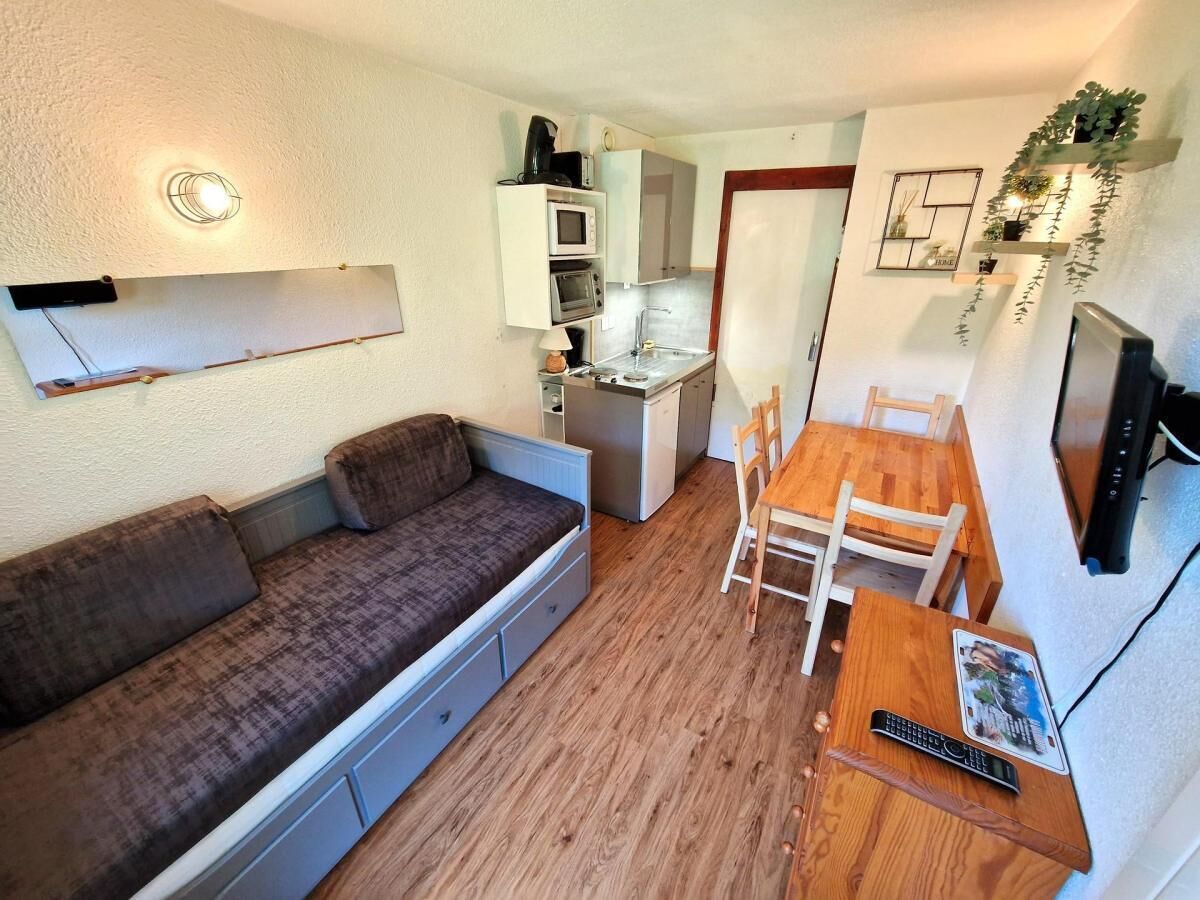 Een ruimtelijk ingerichte leefruimte met een bank, een eettafel met stoelen, een kitchenette en een televisie.