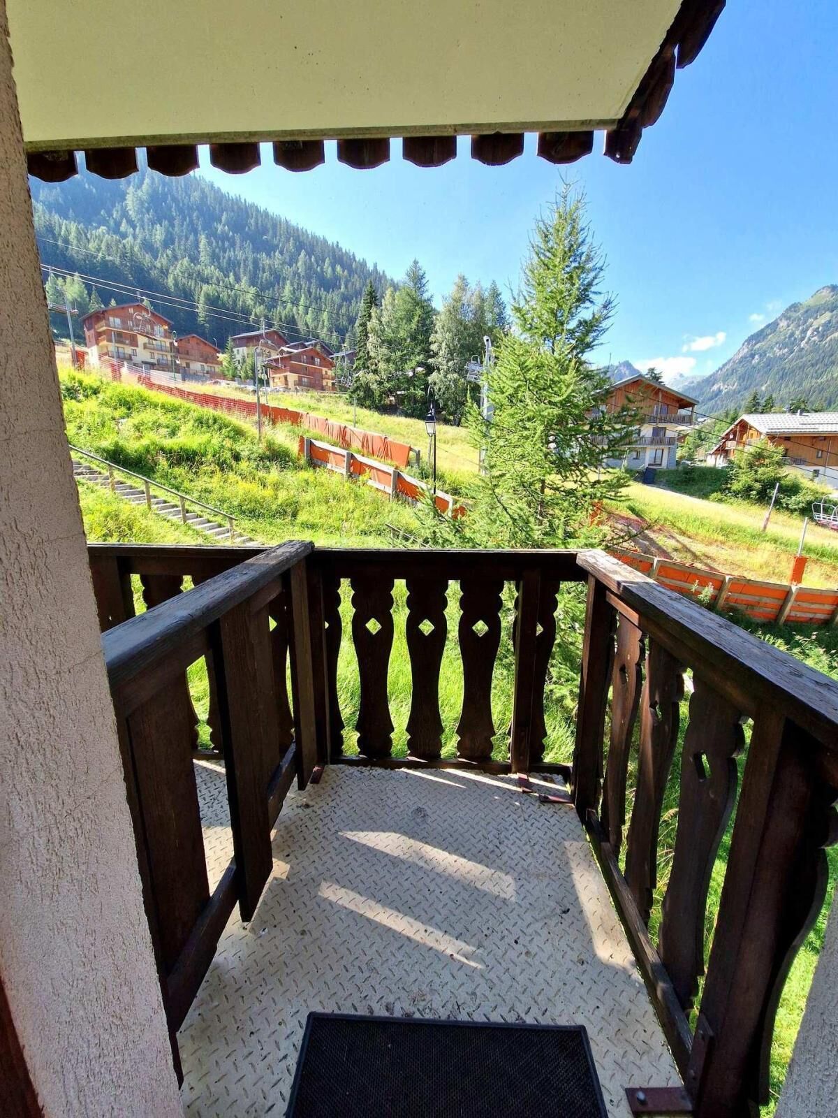 A balcony with a view of a mountainous landscape, wooden railings, and a metal floor.