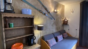 A compact room with a bed, a wooden dresser, a coffee maker, a bowl, and skis mounted on the wall.