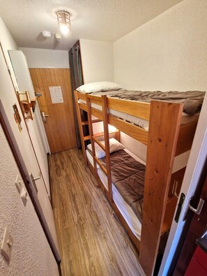 Quarto pequeno com beliche, porta de madeira e uma pequena área de kitchenette.