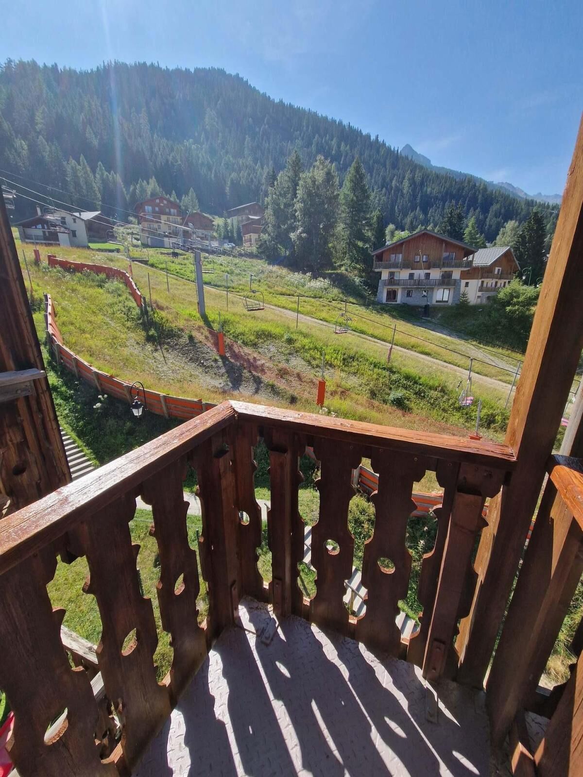 A wooden balcony with a view of a mountain, a ski lift, and houses in the background.