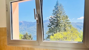 Cozinha com janela dando vista para uma paisagem montanhosa, pia de aço inoxidável, três copos de vinho e uma garrafa sobre o balcão.