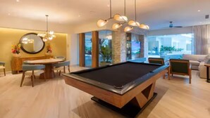 A pool table in a modern living room with a dining area, large windows, and a view of the city. - New beachfront condo with pool and ocean views in welcoming Bucerías (Bucerías)