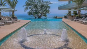 A pool area with a central fountain, lounge chairs, and a view of the ocean. - New beachfront condo with pool and ocean views in welcoming Bucerías (Bucerías)