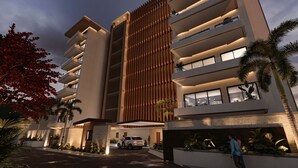 A multi-story hotel with a modern design, featuring balconies, a central vertical wooden panel, and a landscaped entrance. - New beachfront condo with pool and ocean views in welcoming Bucerías (Bucerías)