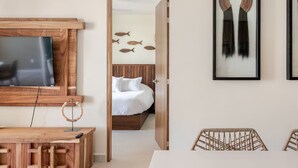 A modern hotel room with a wooden TV stand, a bed with white bedding, a wall-mounted fish decoration, and a framed artwork. - New beachfront condo with pool and ocean views in welcoming Bucerías (Bucerías)