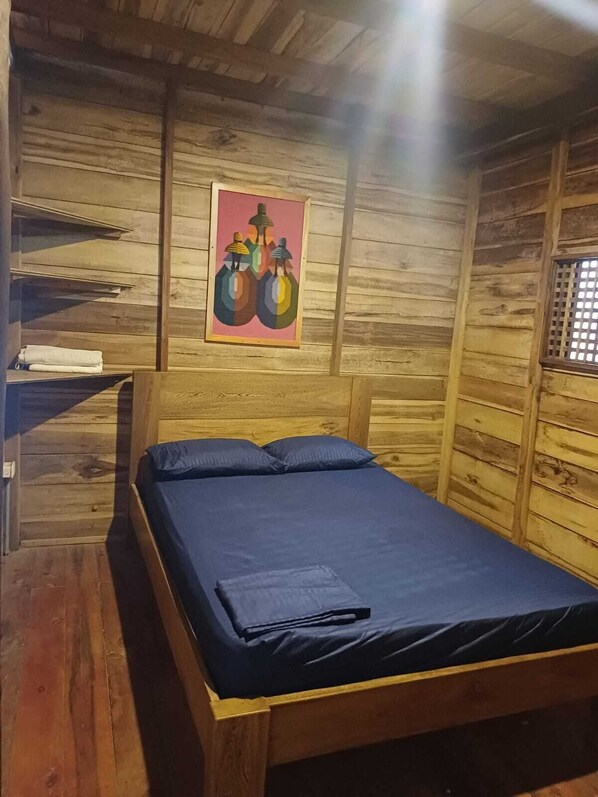 A wooden cabin room with a bed, a window with bars, and a colorful painting on the wall. - Palmbeach (Santa Marta)