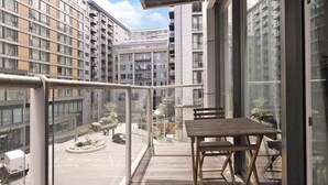 A balcony with a table and chairs, overlooking a parking area and adjacent buildings. - Luxury Apartment at Chelsea Bridge/Battersea Power Station (London)