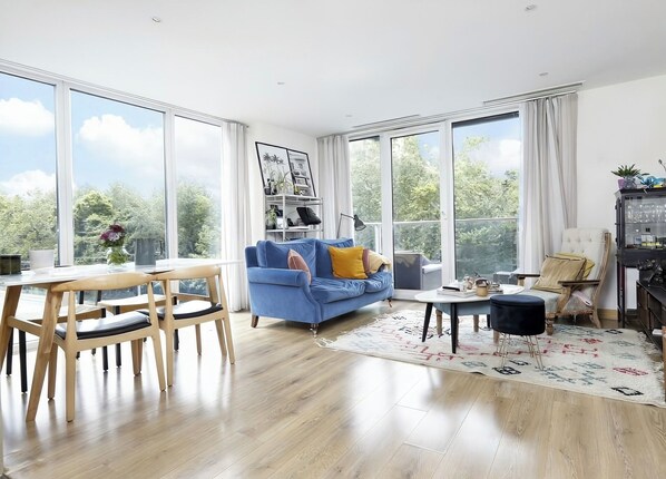 A spacious living room with a blue sofa, wooden dining table, and chairs.