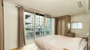 A modern bedroom with a large bed, sliding glass doors leading to a balcony, and a view of the cityscape. - Luxury Apartment at Chelsea Bridge/Battersea Power Station (London)