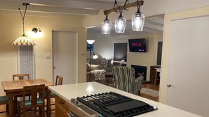 Una cocina moderna con una isla central, una mesa de comedor de madera y sillas. Hay un televisor al fondo y una chimenea.