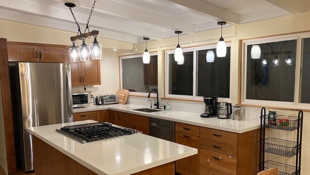 Una cocina moderna con una isla central, electrodomésticos de acero inoxidable, armarios de madera e iluminación colgante.