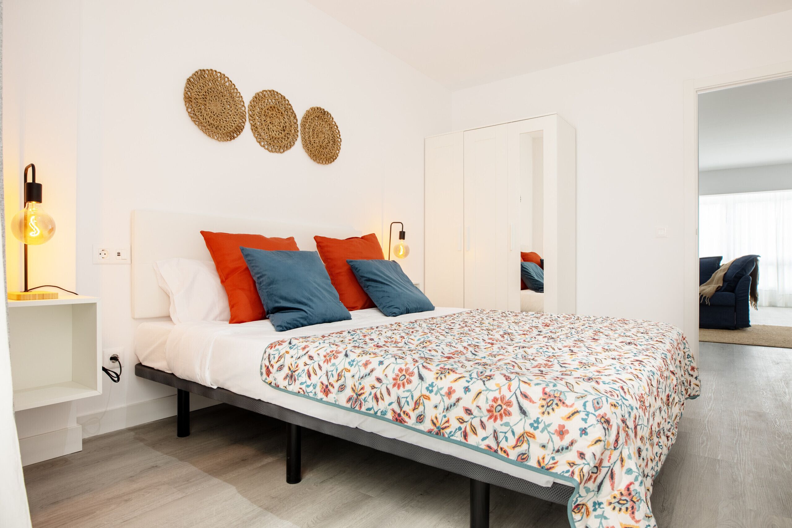 Ein Schlafzimmer mit Bett, Kissen, Nachttischen, einer Wandleuchte und einem Spiegel.