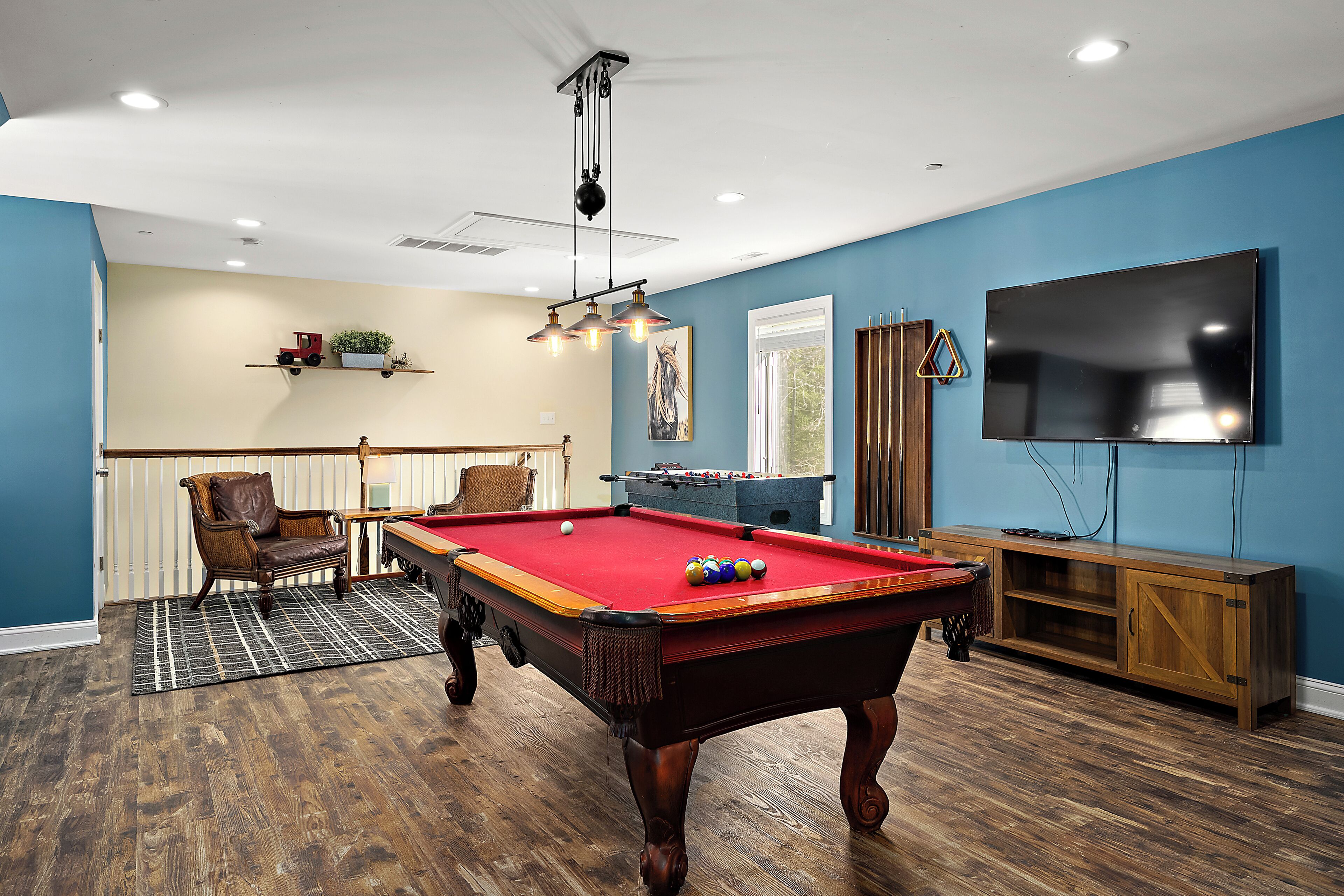A pool table in a room with blue walls, a wooden floor, and a ceiling fan.