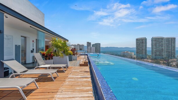Piscina infinita no terraço com espreguiçadeiras, um deck de madeira e um horizonte urbano ao fundo.