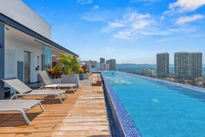 A rooftop infinity pool with lounge chairs, a wooden deck, and a city skyline in the background. - Posh 3-bdr, 2-bath, Parking, Free Airport Shuttle (Puerto Vallarta)