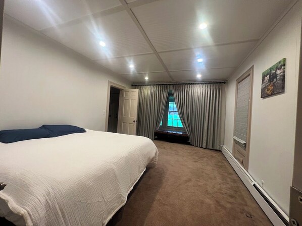 A hotel room with a large bed, a window with curtains, a door, and a wall-mounted artwork.