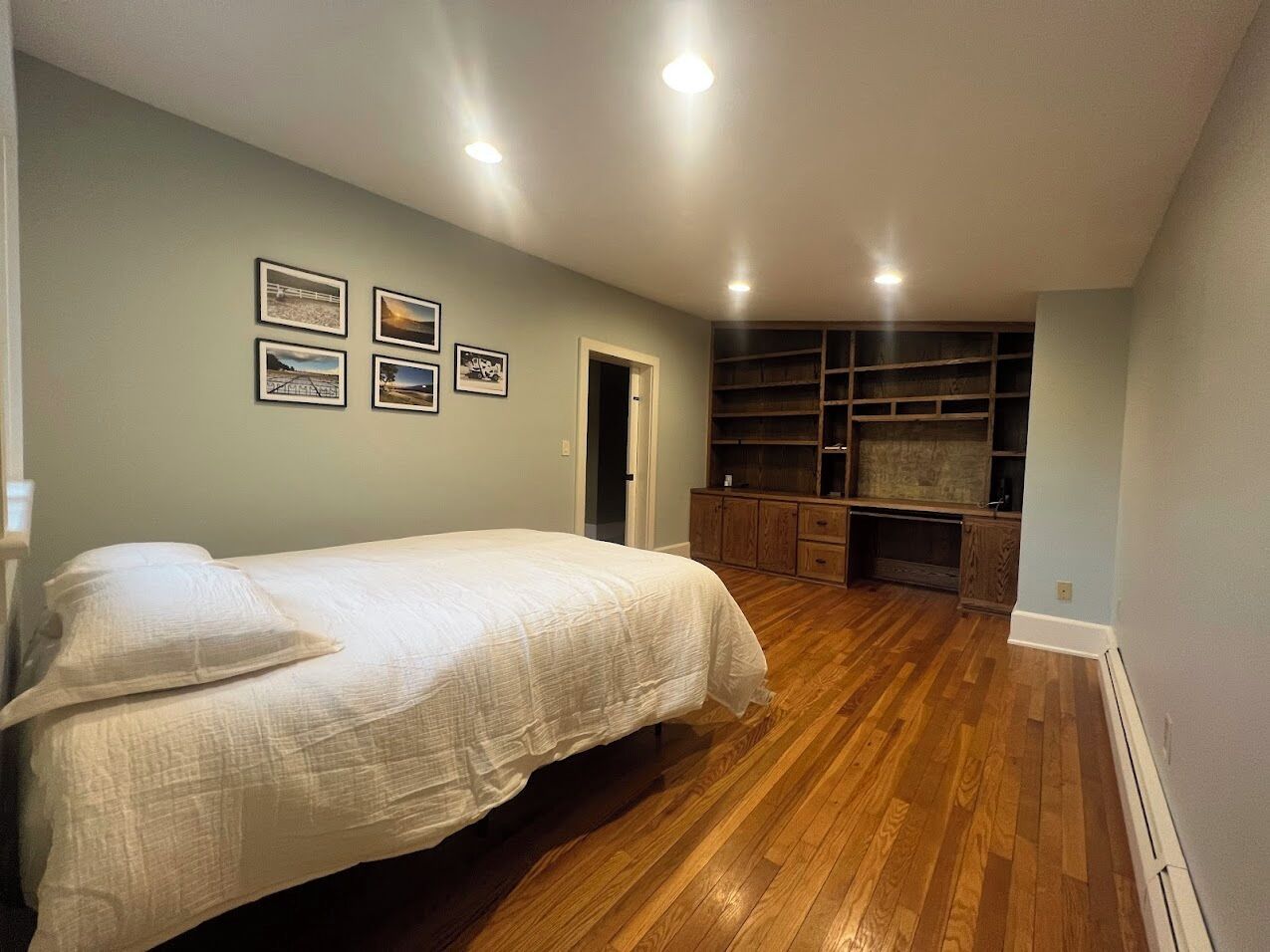 A bedroom with a bed, wooden flooring, built-in shelving, and framed pictures on the wall.