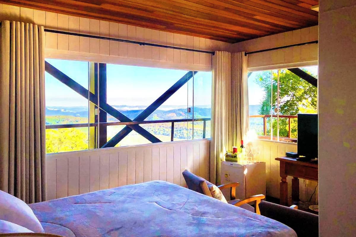 A bedroom with a large window, a bed, a desk, and a television.