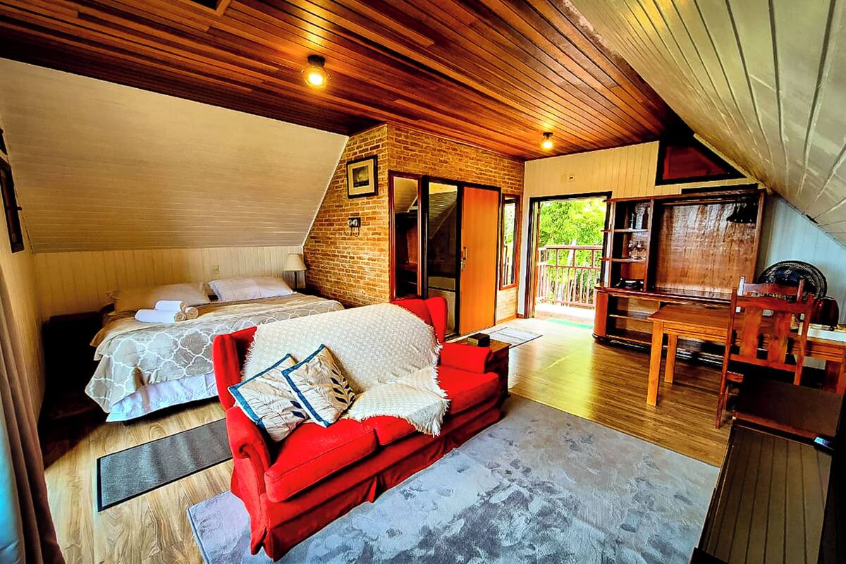 A bedroom with a bed, a red sofa, and a wooden ceiling.