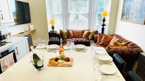 A dining area with a table set for four, a bottle of champagne, and a fruit platter. - Boutique Belmont (Ventnor)