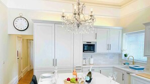A modern kitchen with white cabinets, a chandelier, and a dining table set for six. - Boutique Belmont (Ventnor)