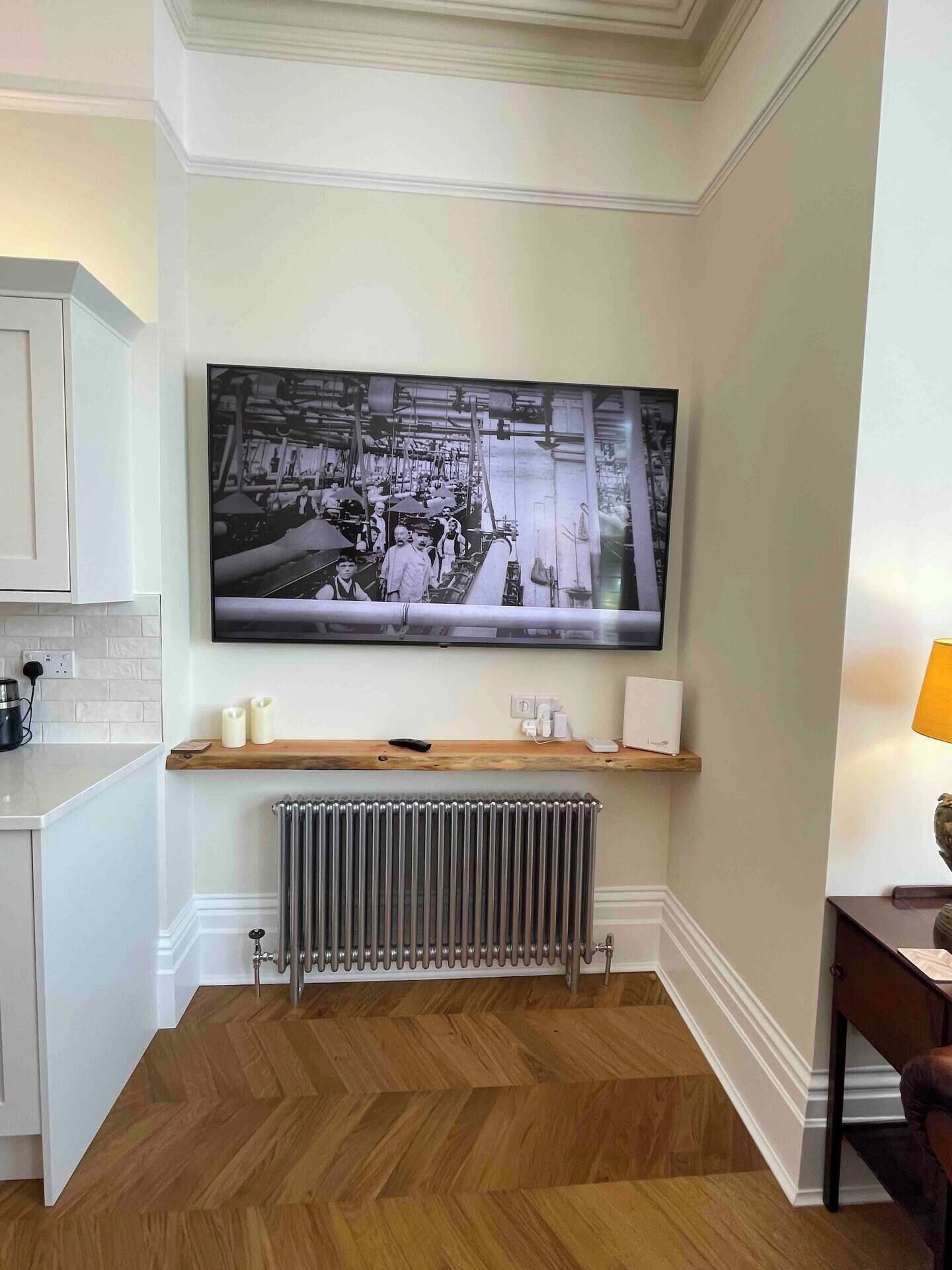 Een moderne keuken met een grote zwart-witfoto aan de muur, een houten plank met kaarsen, een radiator en een visgraat parketvloer.