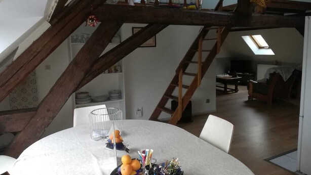 Un coin repas avec une table ronde dressée pour quatre personnes, un escalier en bois et une lucarne au-dessus.