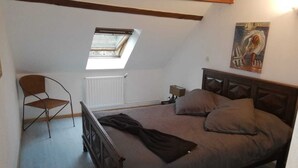 Une chambre avec un plafond en pente, un puits de lumière, un lit avec des oreillers, une chaise et un radiateur.