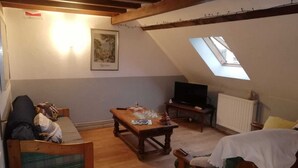 Une pièce mansardée chaleureuse avec un plancher en bois, un canapé, une petite table, un téléviseur et une lucarne.