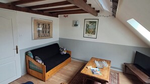 Une pièce chaleureuse avec un canapé en bois, une petite table sur laquelle sont posés des pièces d’échecs et un téléviseur.