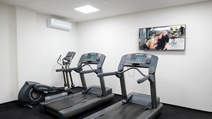 Et fitnessrum med tre løbebånd, en motionscykel og et fjernsyn på væggen.