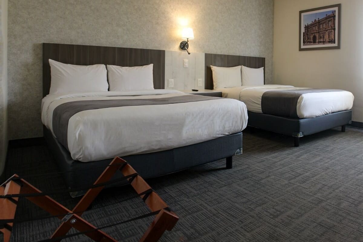 Een hotelkamer met twee bedden, een nachtkastje, een lamp en een lijst met een afbeelding aan de muur.