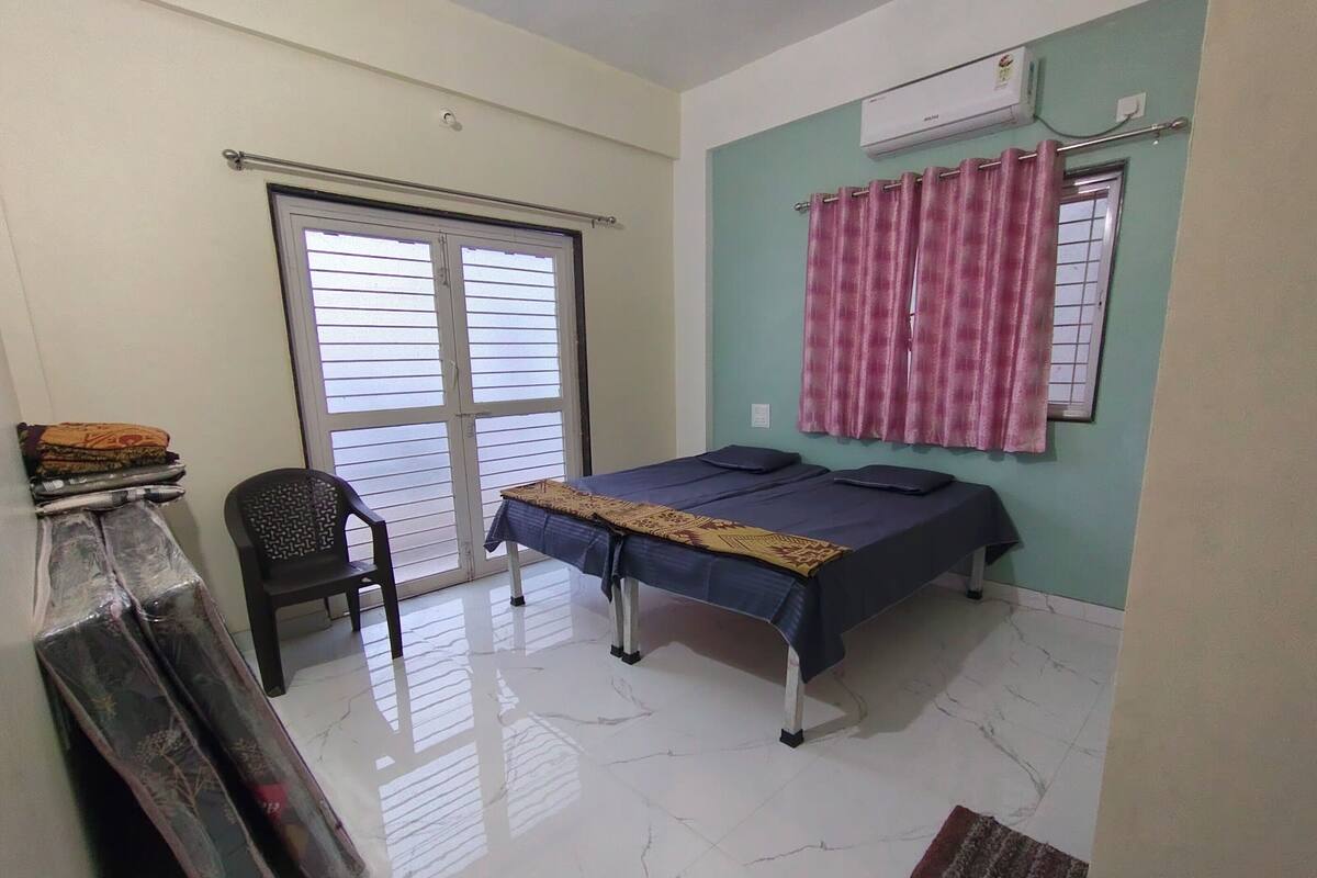 Una habitación pequeña y limpia con una cama, una silla y un ventanal con cortinas.